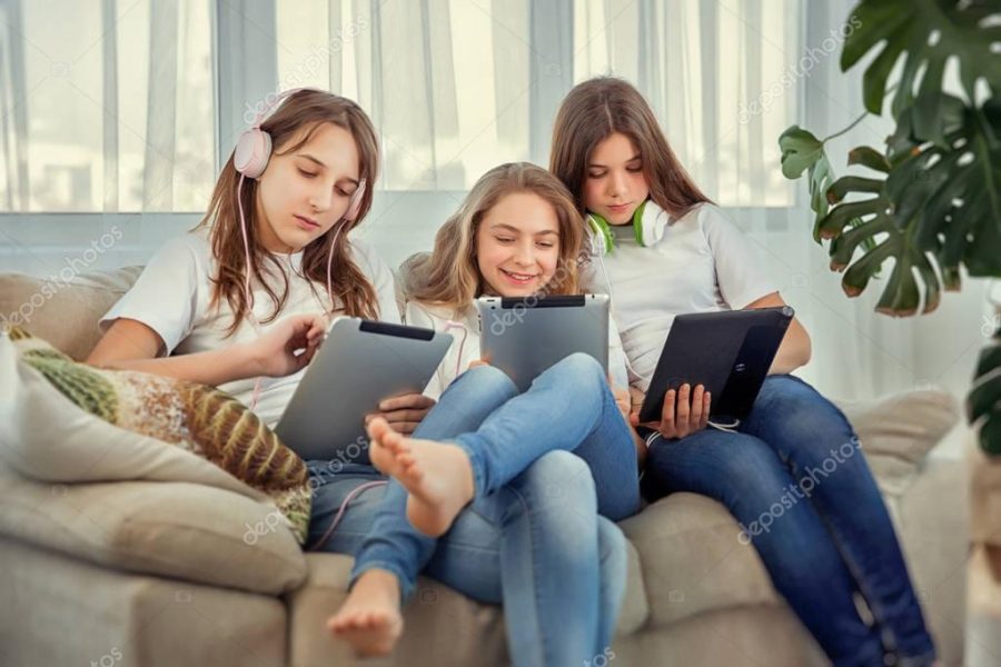 Teenage girls with tablet pc computer and headphones listening music and communicate in social networks