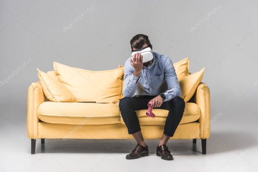 upset man lost in video game with joystick and virtual reality headset on yellow sofa on grey