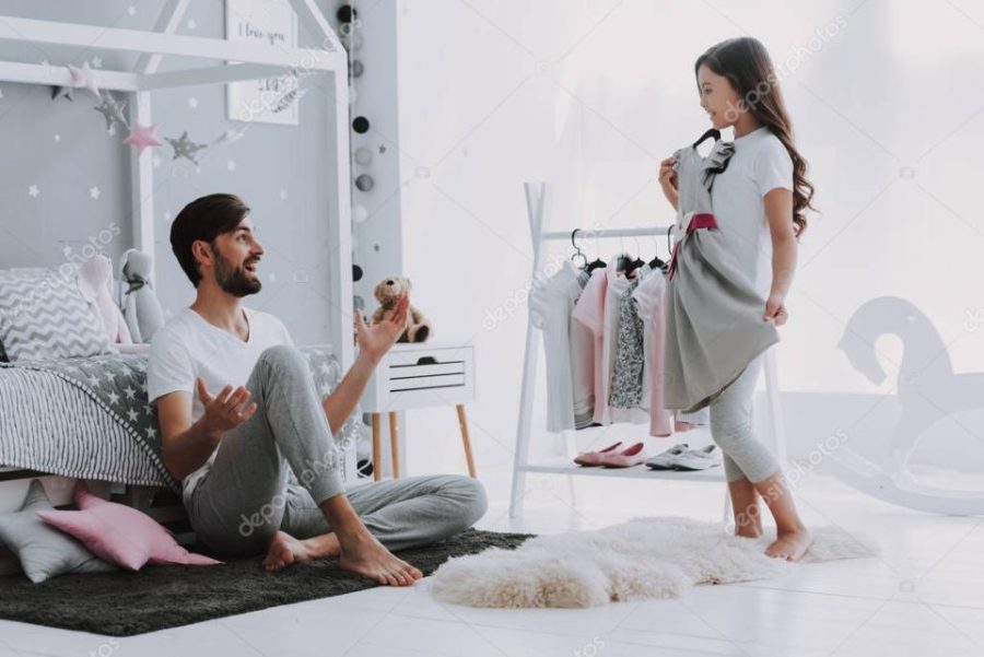 Father Helping Girl Choosing a Dress in Bedroom. Pretty Little Happy Girl Sneaking Among Clothes in Wardrobe. Dress Up Clothes Hanging on a Clothesline for Imagination or Creativity Concept.