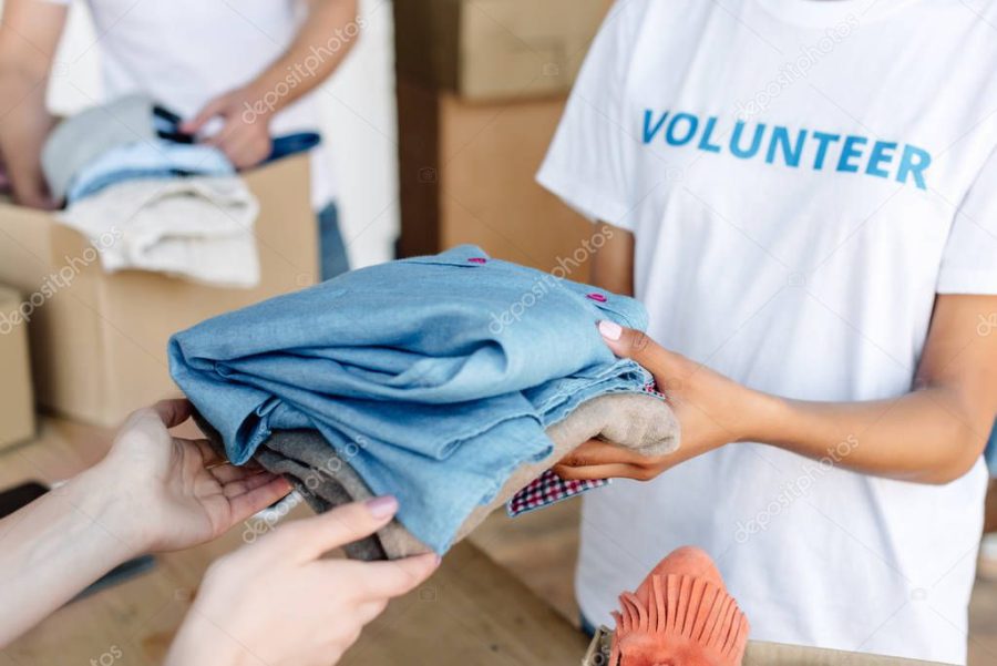 cropped view of volunteer giving clothes to woman in charity center