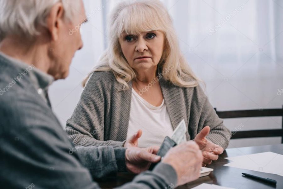 upset senior couple in casual clothes holding money and sitting at table