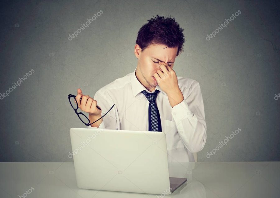 Tired business man rubbing his eye sitting at table with laptop