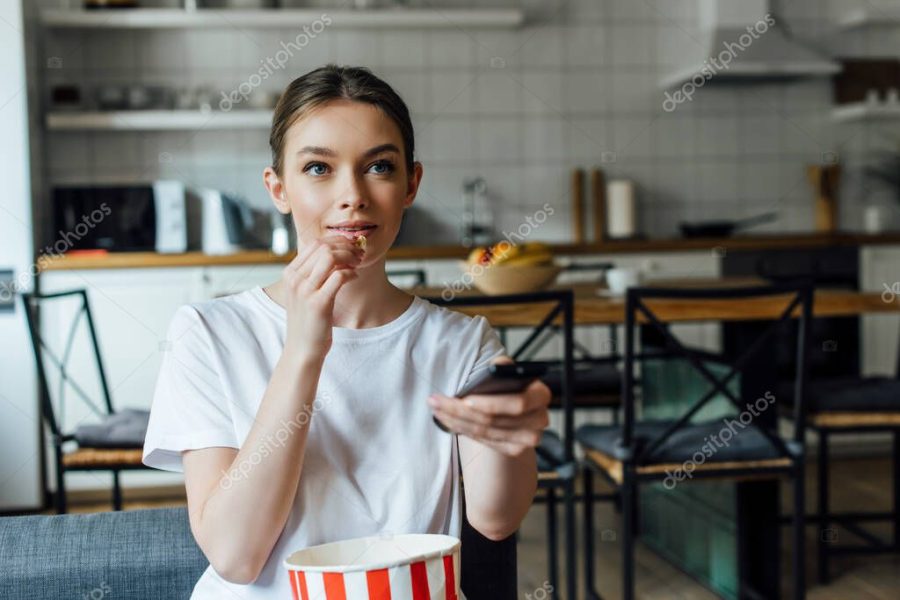 Selective focus of woman eating popcorn and watching movie on sofa