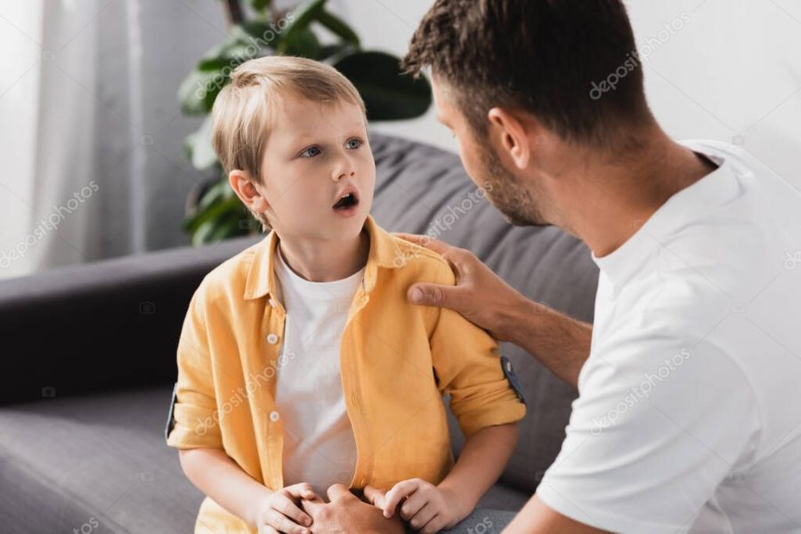 father touching shoulder of socked son while talking to him on sofa