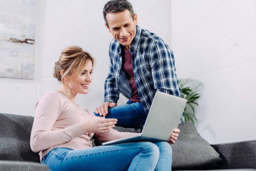 smiling couple using laptop on sofa at home