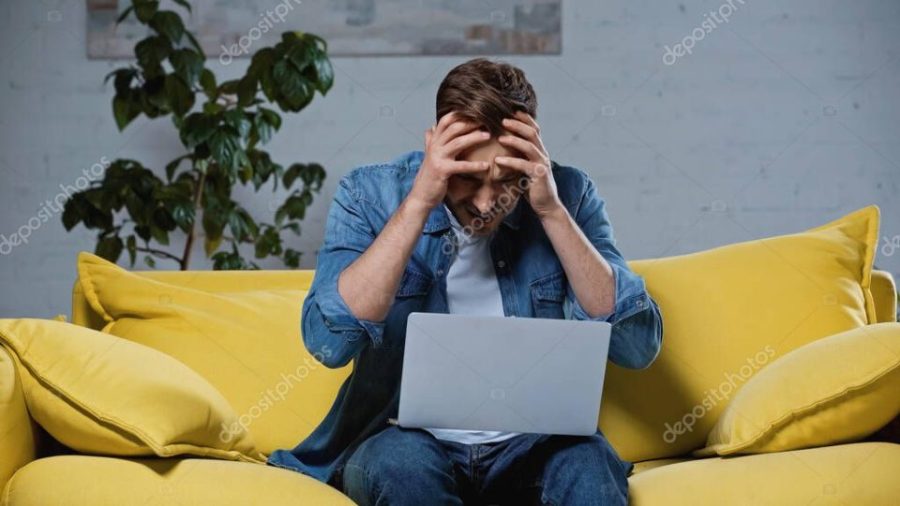 upset freelancer sitting on sofa and touching head while using laptop