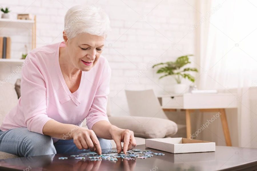 Elderly woman sitting at table and sorting jigsaw puzzle pieces