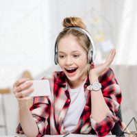 Excited teenager in checkered shirt and headphones smiling during video call
