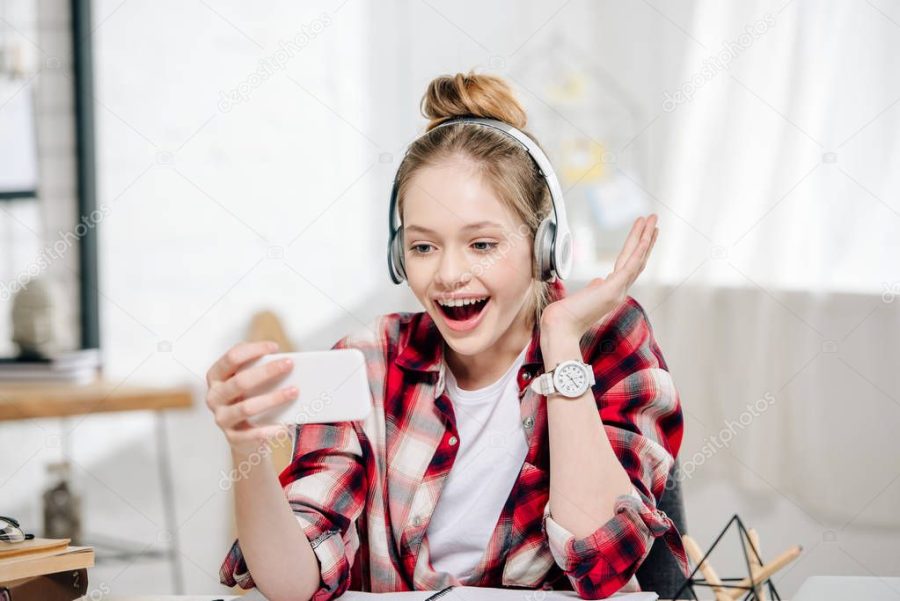 Excited teenager in checkered shirt and headphones smiling during video call