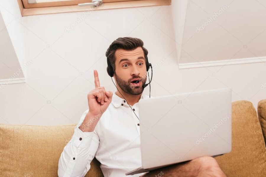 Selective focus of excited freelancer in headset having idea during video chat on laptop at home