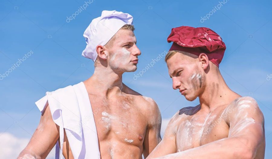 Team of attractive bakers works with flour, preparing dough. Bakers in hats with sexy appearance works together, kneading dough. Brigade of muscular friends works on same shift. Companions concept