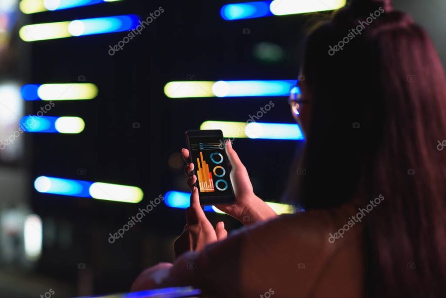 back view of girl holding smartphone with transport appliance on street with neon light in evening, city of future concept