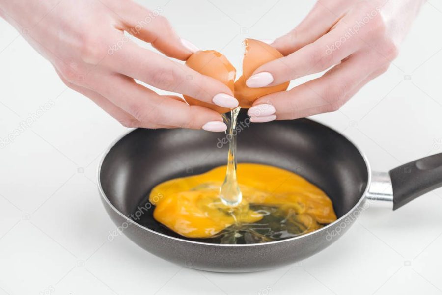 cropped view of woman smashing egg while preparing scrambled eggs in pan on white background