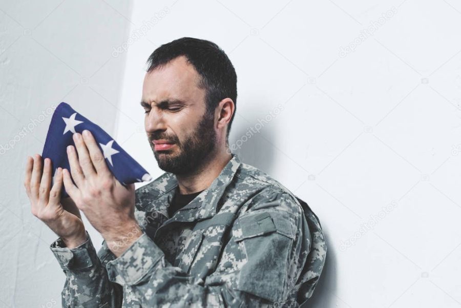 depressed bearded military man crying while sitting by wall and holding usa national flag