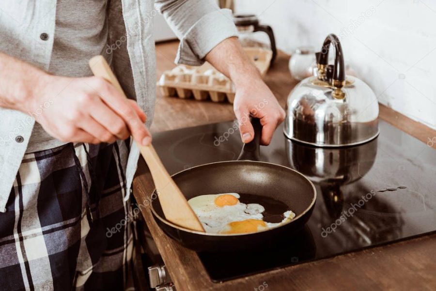 partial view of man cooking scrambled eggs on frying pan in kitchen