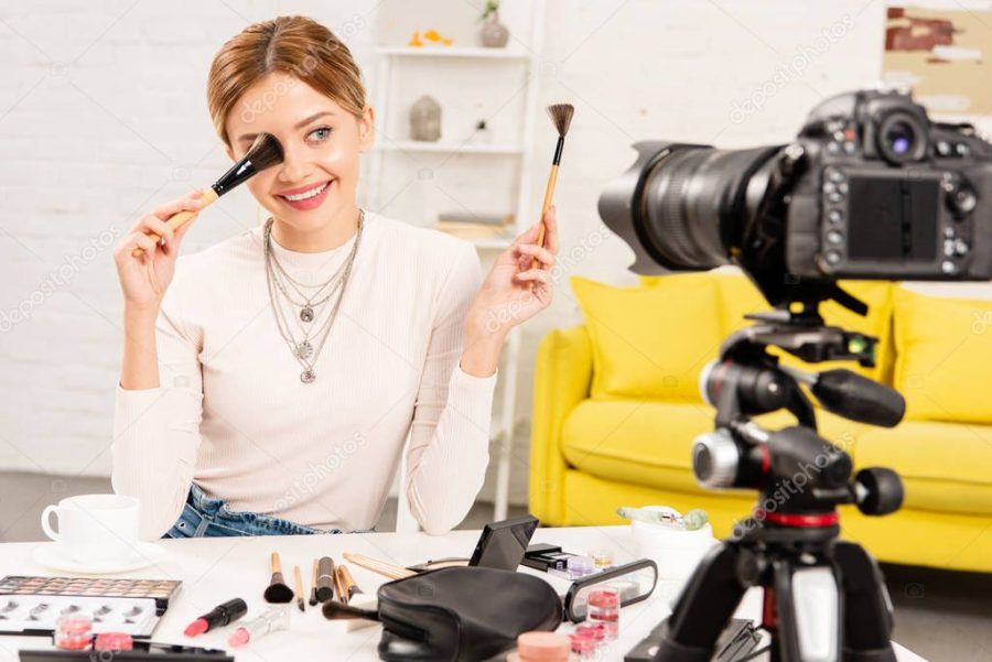 smiling beauty blogger holding cosmetic brushes in front of video camera