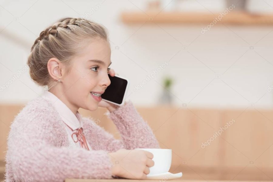 smiling child sitting with cup in hands and using smartphone