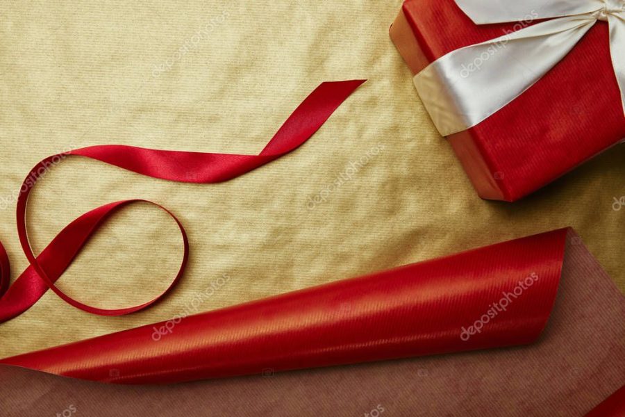 top view of gift and ribbon on red and golden wrapping papers background