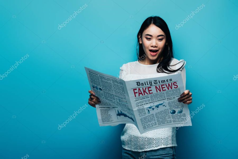 shocked asian woman in white blouse reading newspaper with fake news on blue background