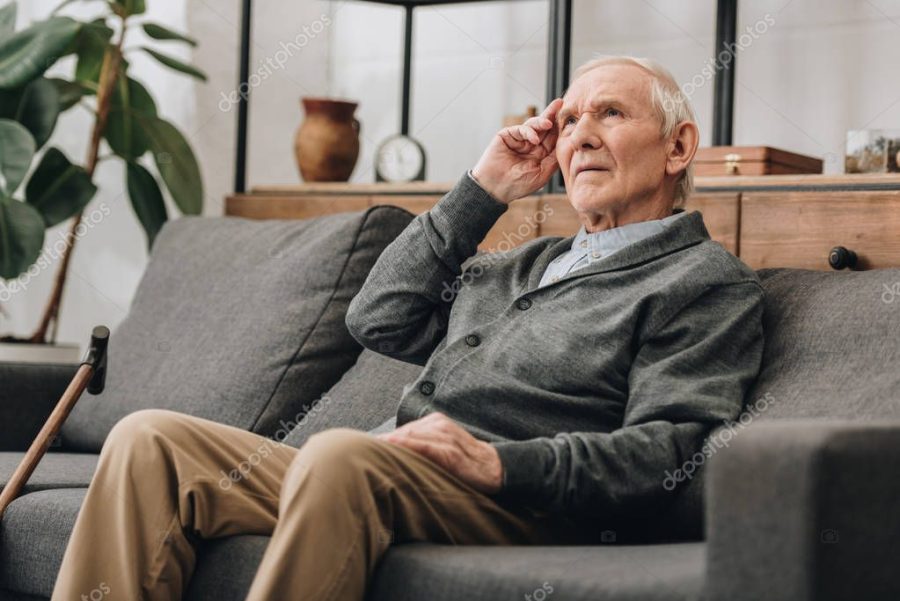 thoughtful senior man with grey hair sitting on sofa in living room