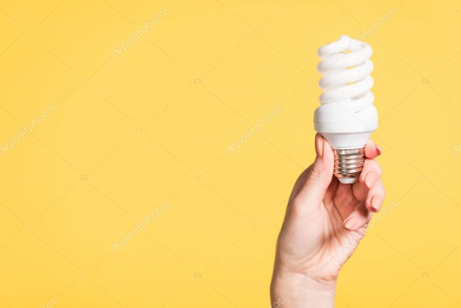 cropped view of female hand holding fluorescent lamp isolated on yellow, energy efficiency concept