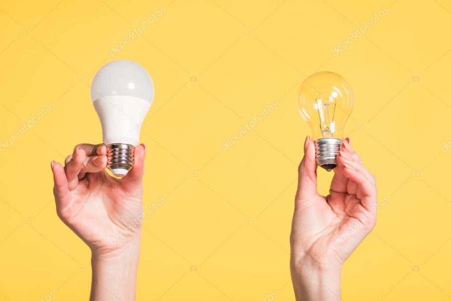 cropped view of female hands choosing between led and fluorescent lamps isolated on yellow, energy efficiency concept