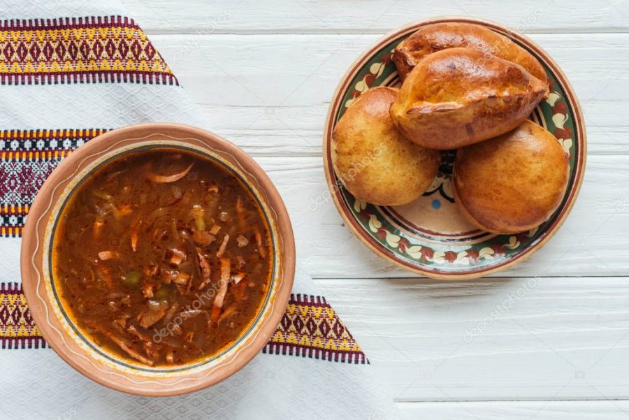 delicious traditional mixed meat soup with mini pies and embroidered towel on white wooden background