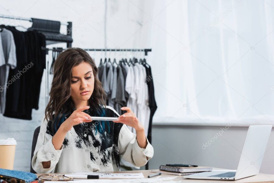 female fashion designer taking picture of painting for print on t-shirt at table