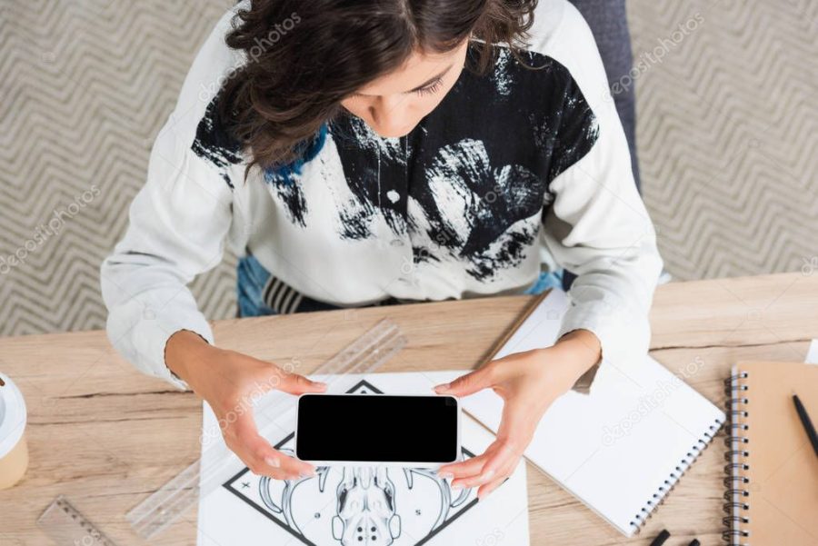 overhead view of female fashion designer taking picture of painting for print on t-shirt at table