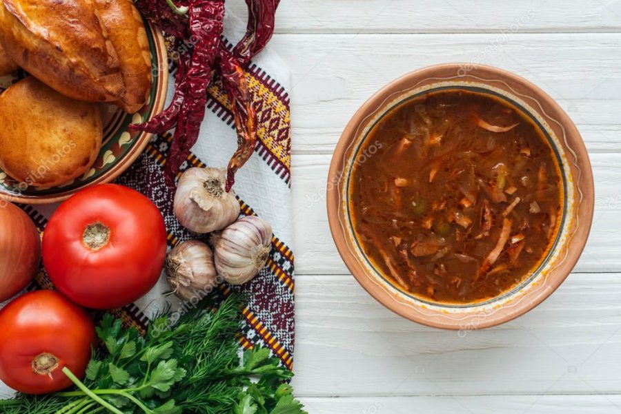 top view of tasty traditional mixed meat soup with mini pies and ingredients on white wooden background