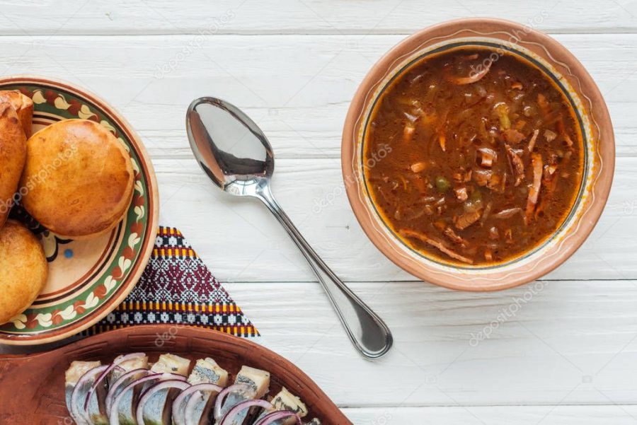 top view of tasty traditional mixed meat soup with mini pies and spoon on white wooden background