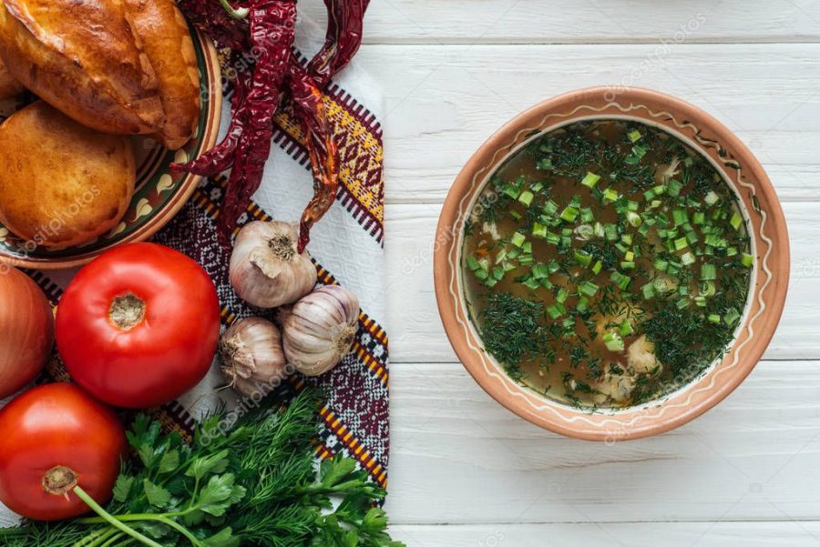 traditional fish soup with green onion, embroidered towel, mini pies and ingredients on white wooden background