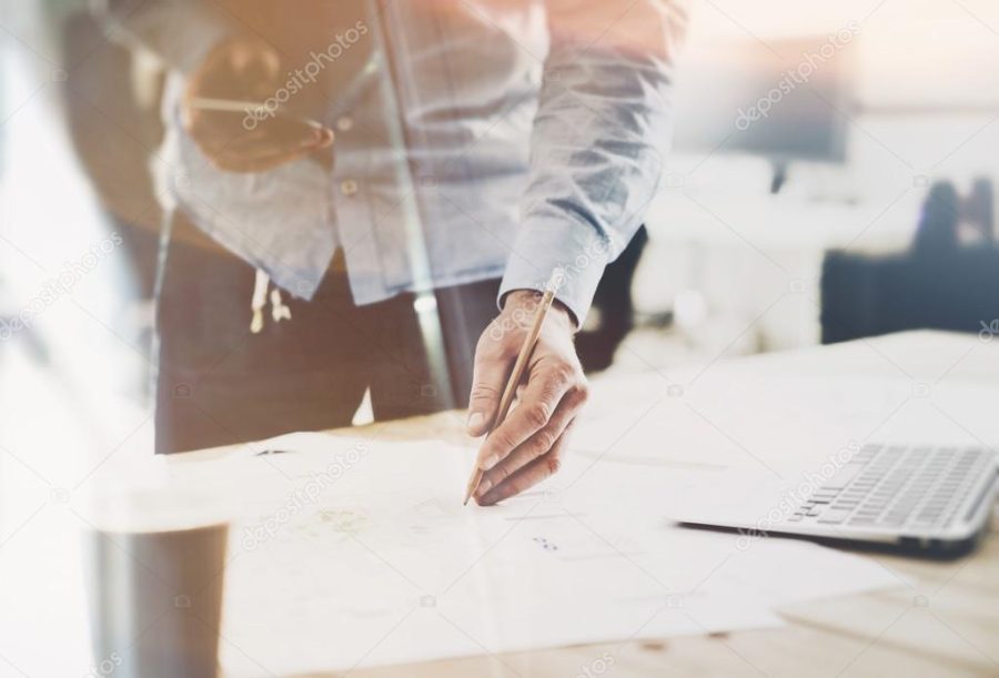 Working process startup. Architect working at the wood table with new building project. Modern notebook on table. Pencil holding hand. Horizontal mockup. Flares, film effect. Blurred background