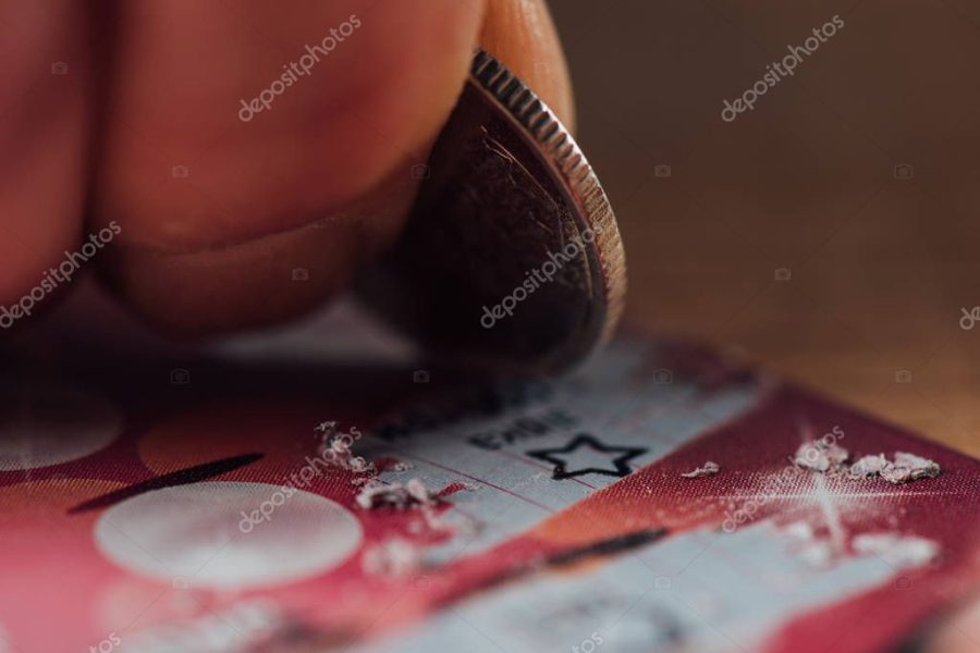 close up view of silver coin in hand of gambler scratching lottery ticket