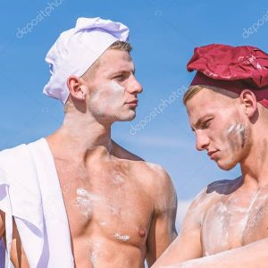 Team of attractive bakers works with flour, preparing dough. Bakers in hats with sexy appearance works together, kneading dough. Brigade of muscular friends works on same shift. Companions concept