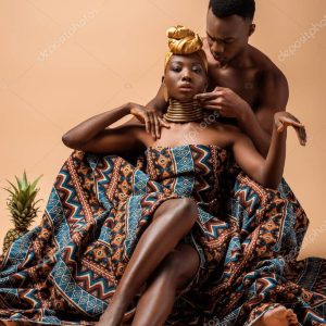 sexy naked tribal afro woman covered in blanket posing near man and pineapple on beige