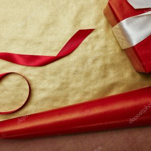 top view of gift and ribbon on red and golden wrapping papers background