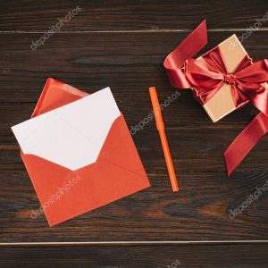 top view of red envelope with blank paper and gift box on wooden table