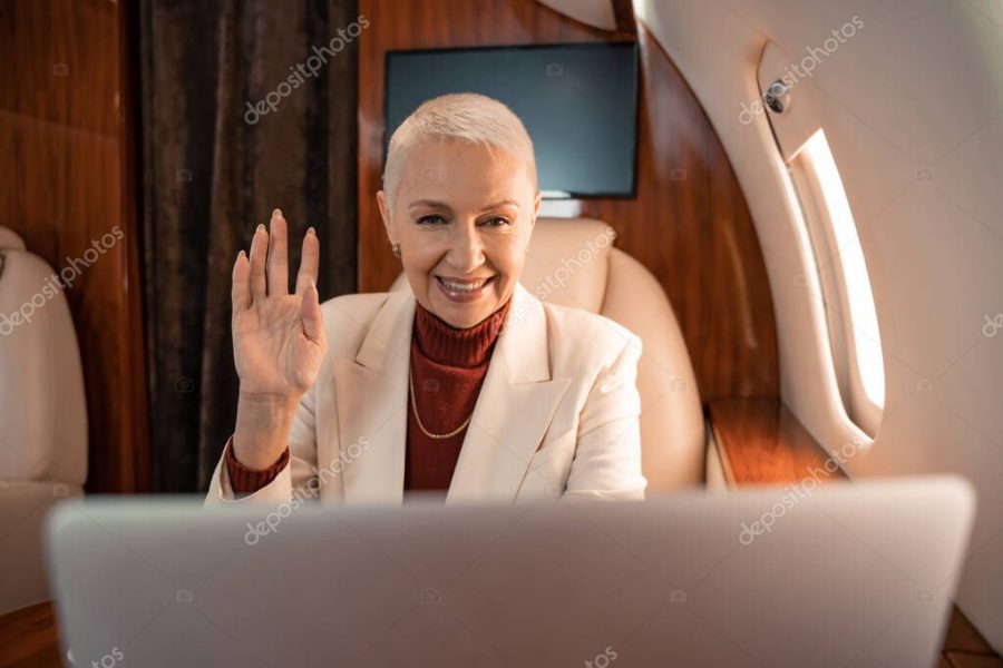 Smiling businesswoman having video call on blurred laptop in plane