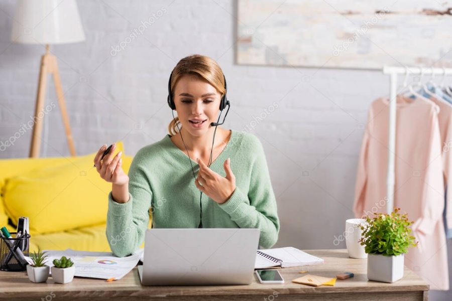 Smiling freelancer with pen using headset during video call on laptop at home