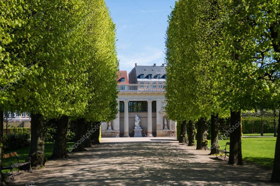 beautiful alley with green trees and historical building with columns and statues in copenhagen, denmark
