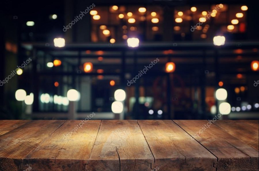 image of wooden table in front of abstract blurred background of resturant lights.