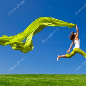 Woman jumping on a green meadow with a colored tissue